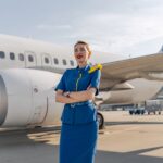 Die schöne Stewardess verschränkte ihre Arme mit weißem Flugzeug auf dem Hintergrund