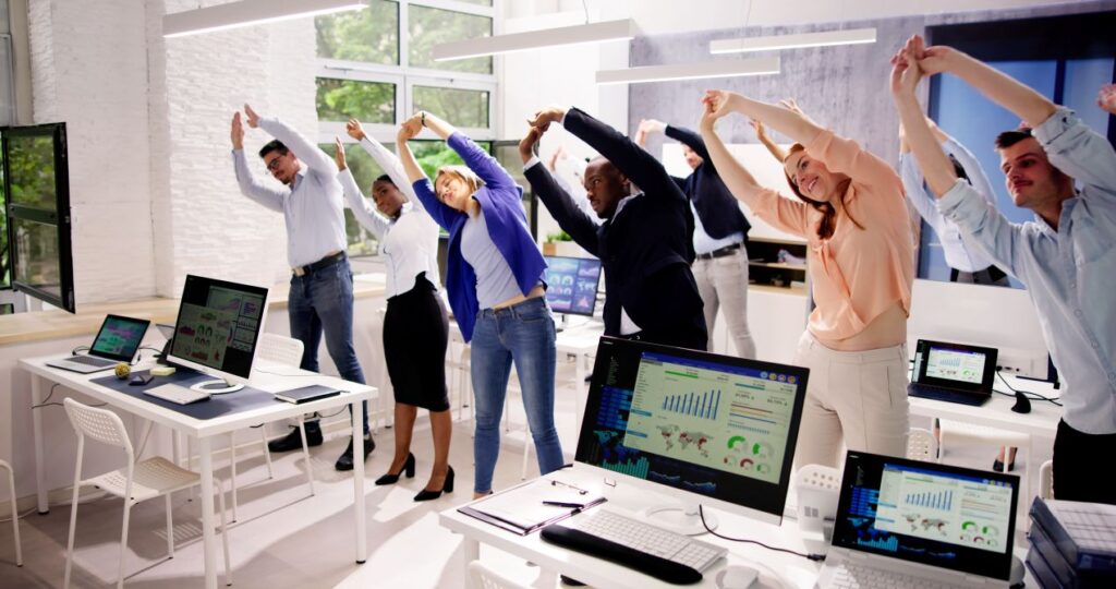 Gruppe von Bueroangestellten dehnt sich gemeinsam im Office – Bewegungsroutine mit personal trainer koeln fuer mehr Gesundheit im Arbeitsalltag